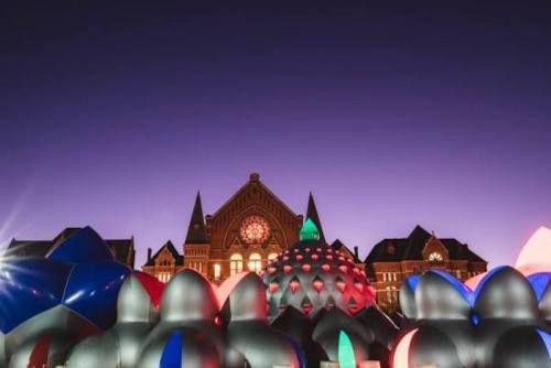 Colorful inflatable structures in the foreground with a historic building and twilight sky in the background.