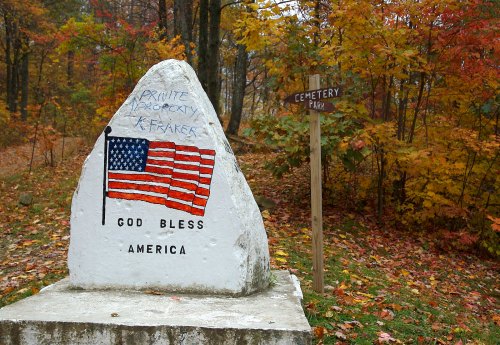 A painted rock with an American flag and "God Bless America" surrounded by autumn foliage and a sign for Cemetery Park.
