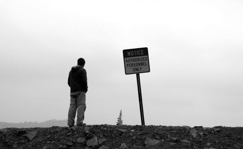 A person stands on a rocky ledge, facing a sign that reads "Notice: Authorized Personnel Only" against a gray sky.