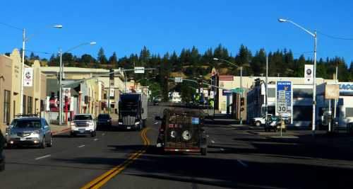 A view of a small town street with shops, traffic lights, and a truck driving down the center lane under a clear blue sky.