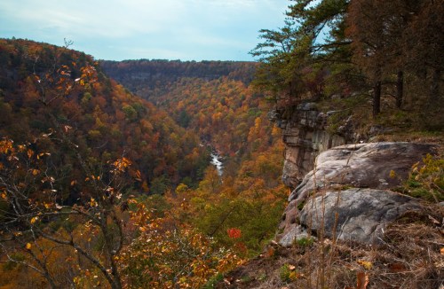 A scenic view of a valley with colorful autumn foliage and a winding river below rocky cliffs.