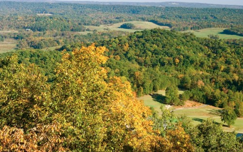 A scenic view of rolling hills and trees with autumn foliage, overlooking a green valley and golf course below.