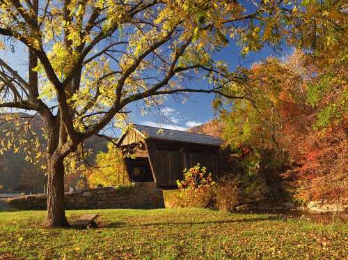 A scenic view of a covered bridge surrounded by colorful autumn foliage and a tranquil river.