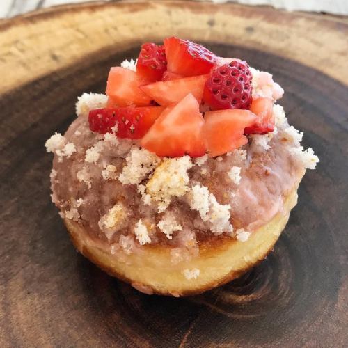 A delicious donut topped with strawberry pieces and crumbled cake on a wooden surface.