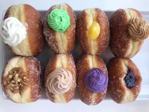 A tray of nine assorted donuts, each topped with colorful frosting and fillings, arranged in three rows.
