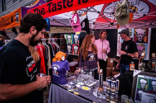 A lively market scene with vendors showcasing craft beer, merchandise, and art under colorful tents.