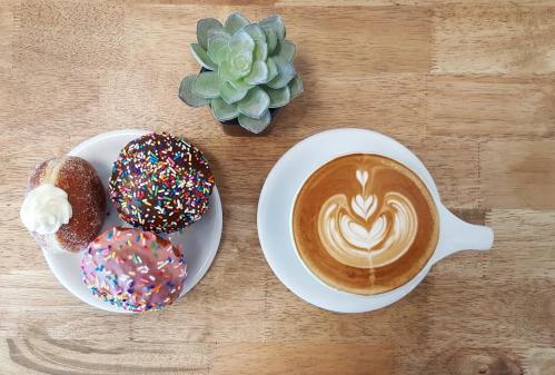 A plate of colorful donuts beside a latte with heart art, accompanied by a small succulent plant on a wooden table.