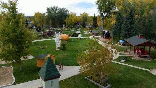 Aerial view of a park with walking paths, trees, playgrounds, and colorful structures in a vibrant green landscape.