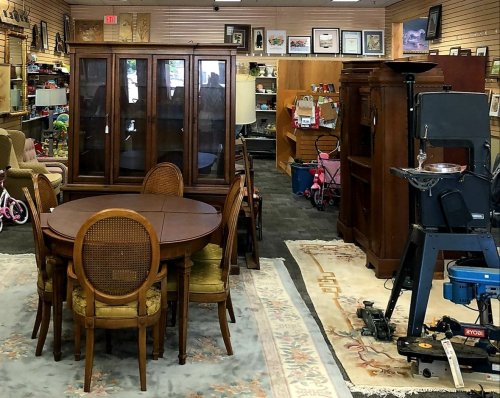 A cozy thrift store interior featuring a dining table, chairs, cabinets, and various furniture items.