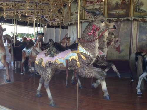 A whimsical carousel featuring intricately designed animals, including a goat adorned with a pink bow.