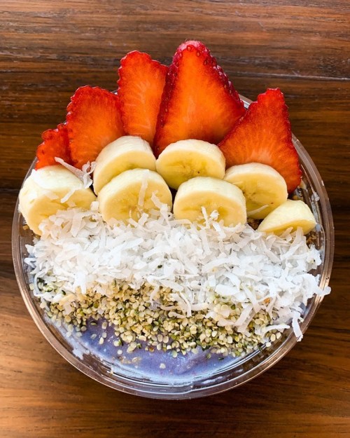 A colorful smoothie bowl topped with sliced strawberries, bananas, shredded coconut, and hemp seeds.