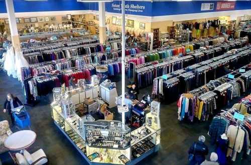 A spacious thrift store filled with racks of clothing and a display of accessories in the center.