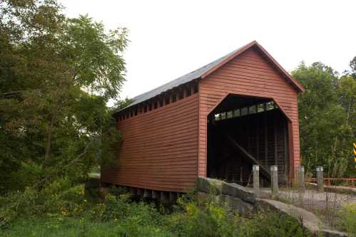 A red covered bridge stands over a small stream, surrounded by trees and greenery.