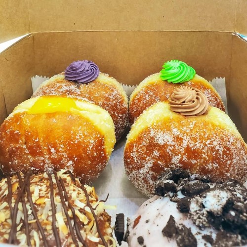 A box of assorted donuts: two with purple and green frosting, one with yellow filling, and one topped with chocolate and nuts.