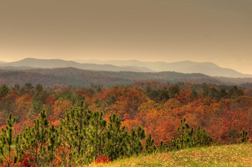 A scenic view of autumn foliage with rolling hills and mountains in the background under a hazy sky.