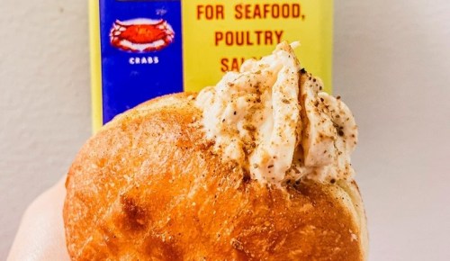 A close-up of a bun filled with crab meat, with a can of crab seasoning in the background.