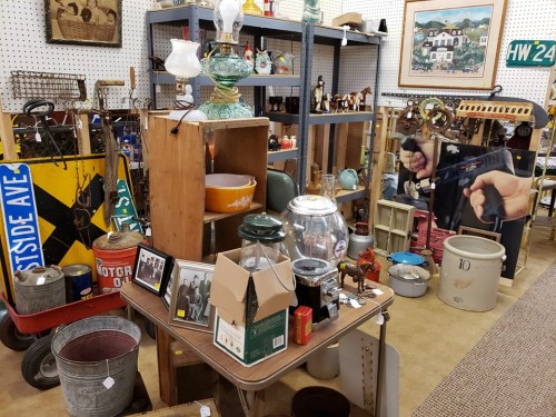 A cluttered antique shop filled with various vintage items, including lamps, jars, and decorative objects on display.