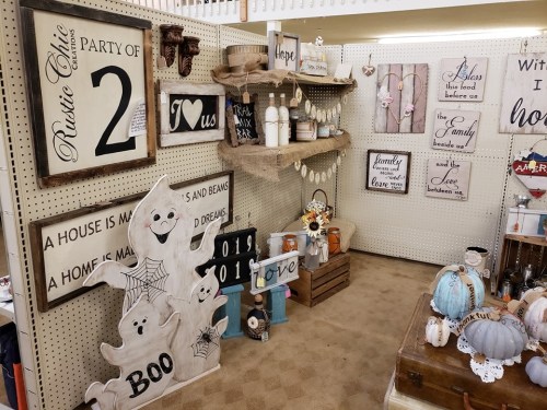 A cozy display of rustic home decor, featuring signs, ghost decorations, and seasonal items in a charming shop setting.