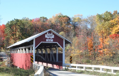A red covered bridge surrounded by vibrant autumn foliage and trees in various fall colors.