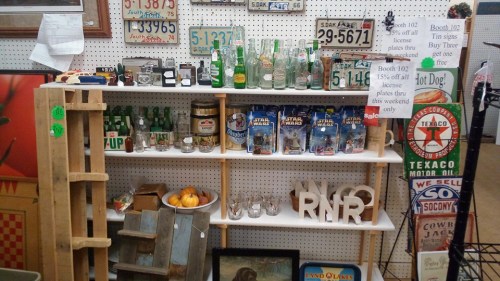A display shelf with vintage bottles, signs, and decorative items, including a wooden crate and oranges.