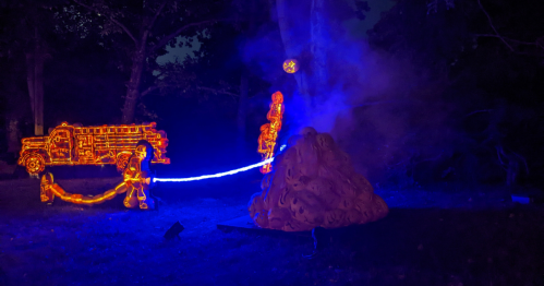 A glowing fire truck and firefighters battling a colorful, illuminated fire in a dark outdoor setting.