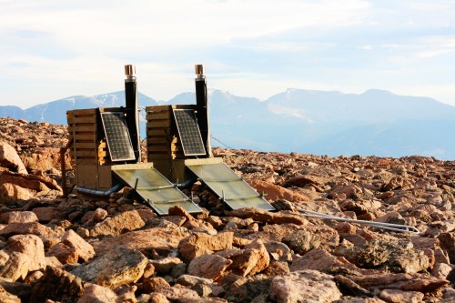 Two solar panels set on rocky terrain with mountains in the background under a clear sky.