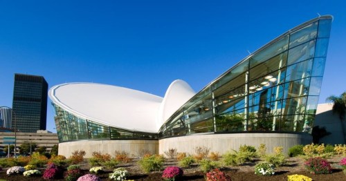 Modern building with a unique, curved design and large glass windows, surrounded by colorful flowers and clear blue sky.