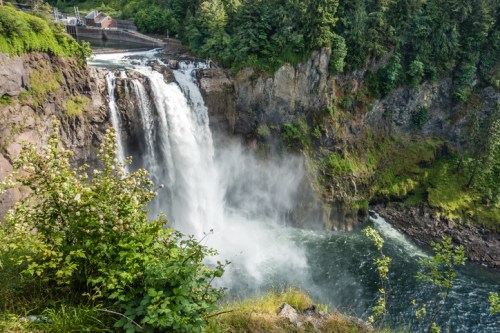 A scenic view of a waterfall cascading into a river, surrounded by lush greenery and rocky cliffs.