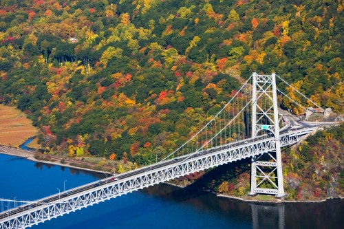 Aerial view of a white suspension bridge over a river, surrounded by vibrant autumn foliage.