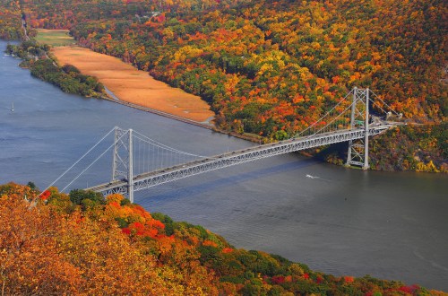 Aerial view of a bridge spanning a river, surrounded by vibrant autumn foliage in shades of orange and yellow.