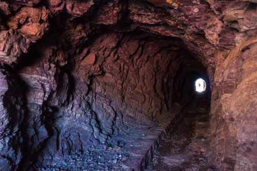 A dark tunnel with rocky walls, leading to a bright light at the far end, creating a sense of depth and mystery.