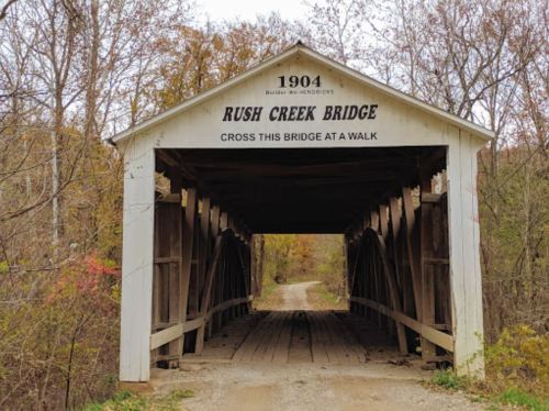 A covered bridge with a sign reading "Rush Creek Bridge" and the year "1904," surrounded by autumn foliage.