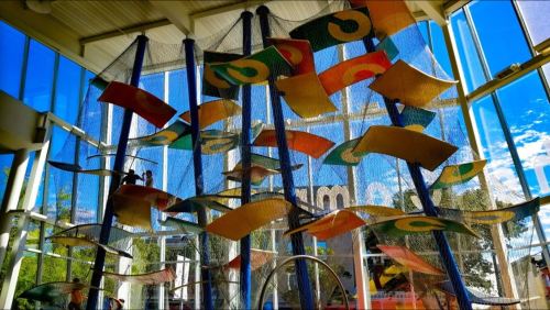 Colorful suspended panels create a playful installation in a bright, airy space with large windows.