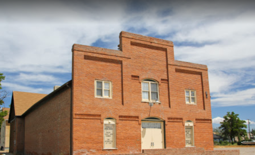 A brick building with a flat roof, featuring windows and a door, set against a blue sky with clouds.
