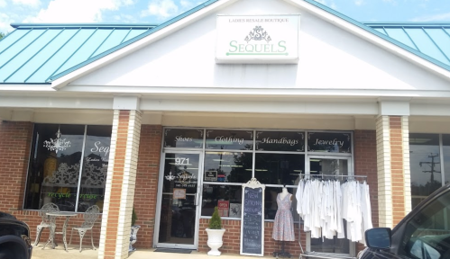 Exterior of a boutique named "Sequels," featuring clothing, shoes, handbags, and jewelry, with a blue roof and white dresses displayed.