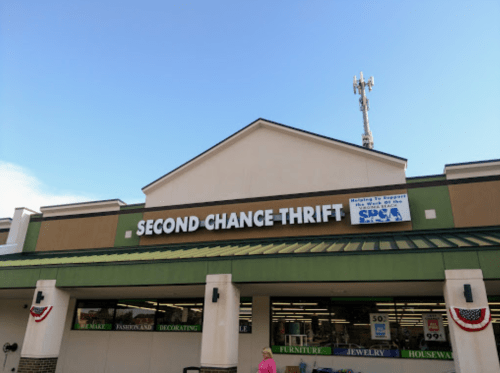 Exterior of a thrift store named "Second Chance Thrift," featuring a clear blue sky and decorative flags.