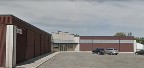 A large commercial building with a flat roof and a parking lot, featuring a mix of red and gray exterior walls.