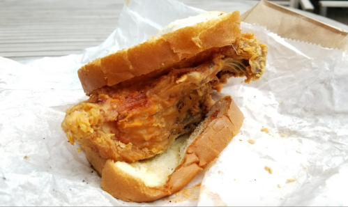 A fried chicken sandwich with a crispy chicken piece between two slices of bread, resting on crumpled paper.