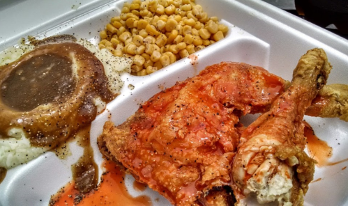 A takeout container with fried chicken, mashed potatoes with gravy, and corn.