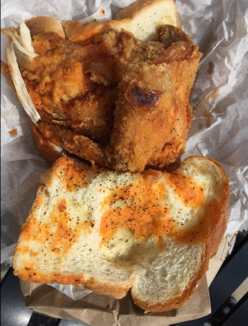 A close-up of a sandwich with fried chicken and spicy sauce on two slices of white bread, resting on crumpled paper.
