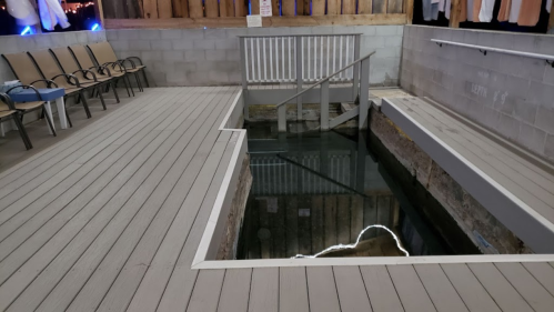 A wooden deck with a pool area featuring stairs leading down to the water, surrounded by seating.