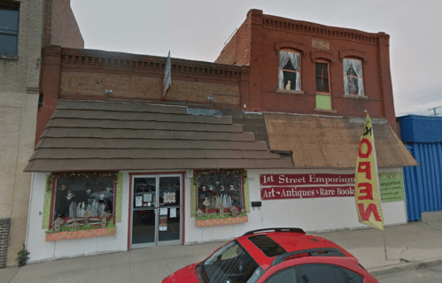 A vintage storefront with a sloped roof, colorful window displays, and a large "OPEN" flag outside.