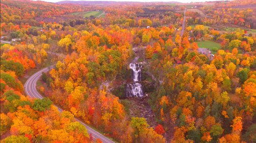 Aerial view of a vibrant autumn landscape with colorful trees and a waterfall surrounded by rolling hills.