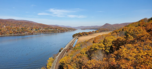 A scenic view of a river surrounded by autumn foliage and rolling hills under a clear blue sky.