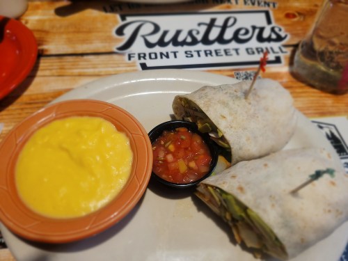 Two wrapped burritos with a side of yellow cheese dip and salsa on a wooden table with a restaurant logo.