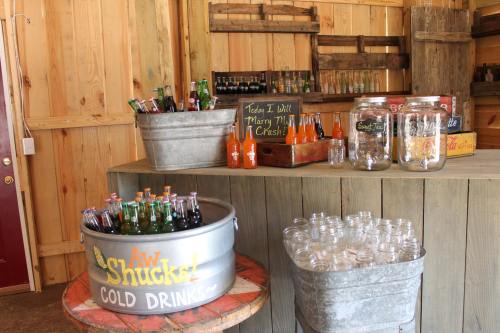 A rustic drink stand featuring metal tubs of soda bottles and jars, set against a wooden backdrop.