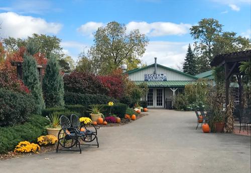 A scenic view of Becker Brewing with colorful flowers, pumpkins, and trees lining the pathway under a blue sky.