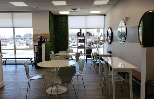 A modern, bright café interior with green accents, round mirrors, and various seating options.