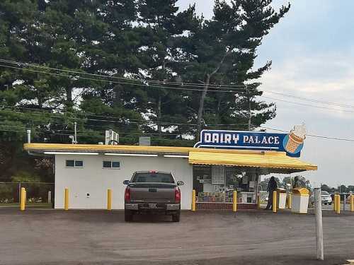 A small ice cream shop named "Dairy Palace" with a yellow roof and a pickup truck parked outside. Pine trees in the background.