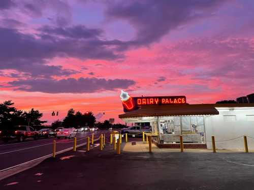 A colorful sunset over Dairy Palace, featuring a neon ice cream cone sign and parked cars along the road.